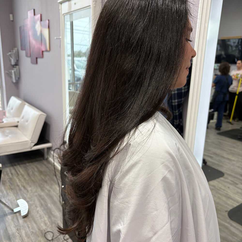 Woman with long, wavy brown hair at a salon, seated on a white couch.