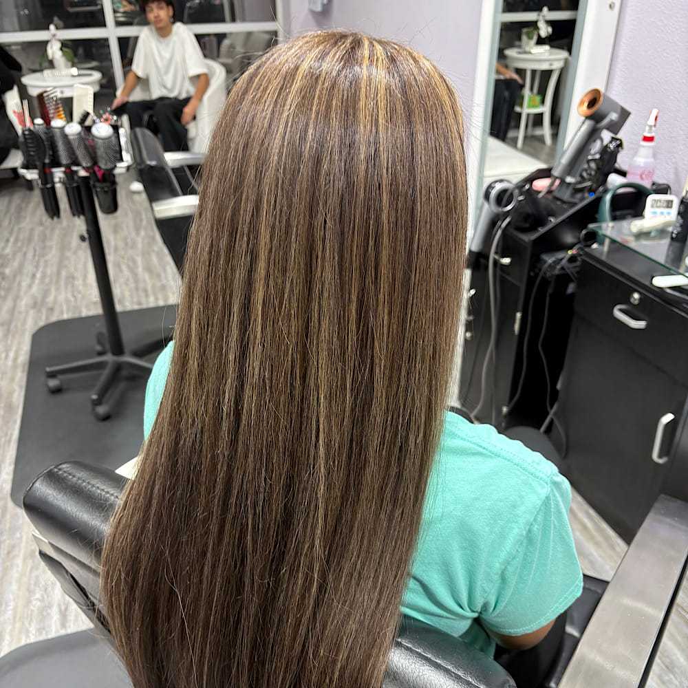 Long brown hair with highlights in a salon chair, haircut tools on counter.