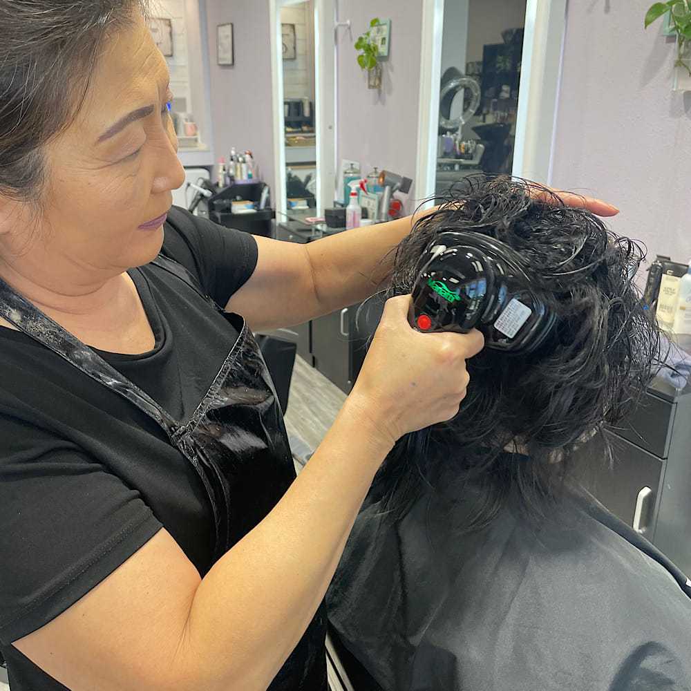 Hairstylist applying treatment to a client's wet hair in a salon setting.