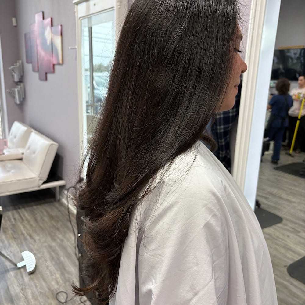 Woman with long, wavy brown hair at a salon, seated on a white couch.