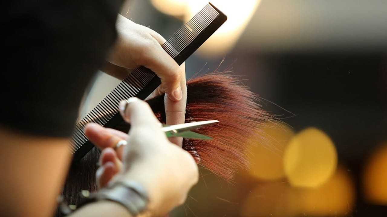 Person cutting hair with scissors and comb in a salon setting.